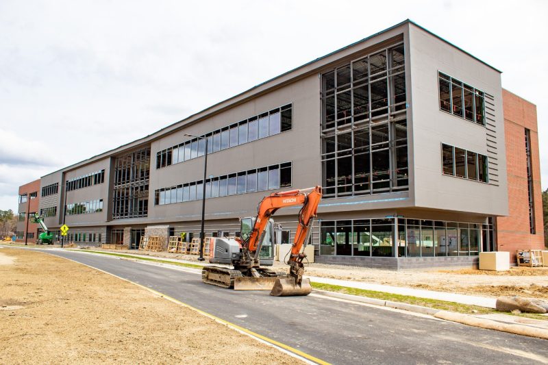 A partially constructed modern three-story office building with construction equipment sitting in the foreground.