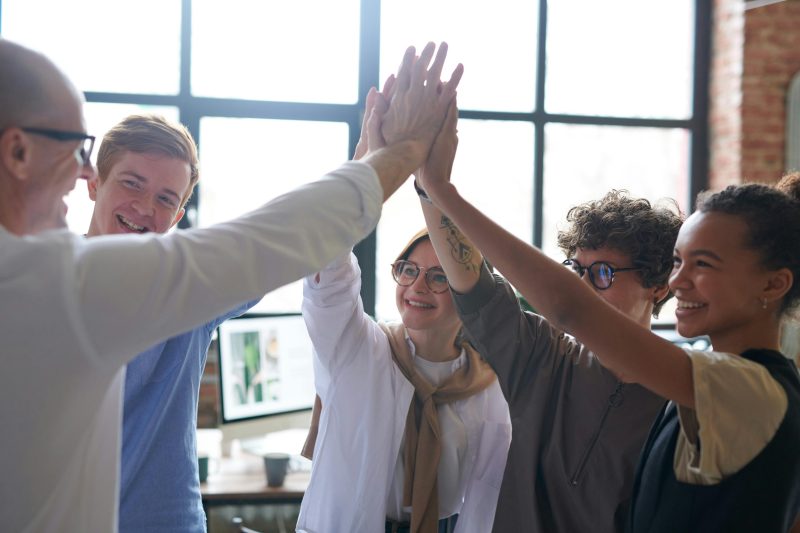 A group of five people stand in a circle with their hands lifted to the center in a giant high-five.